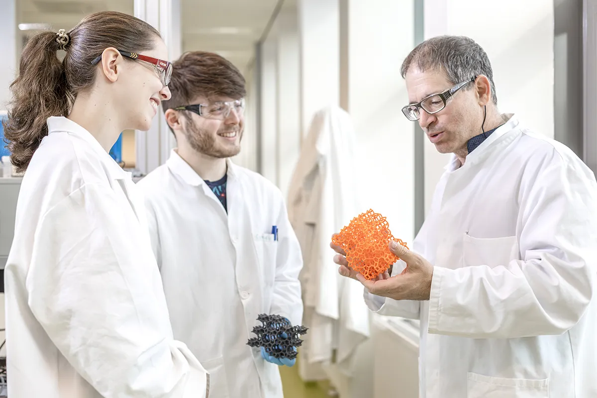 Drie onderzoekers in witte labjas bespreken een model in een modern laboratorium