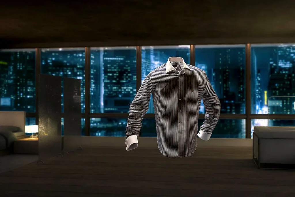 Een netjes geperst, gestreept overhemd hangt in de lucht in een modern, slecht verlicht appartement met grote ramen. Het nachtelijke stadsbeeld dat door de ramen zichtbaar is, bestaat uit hoge gebouwen met gloeiende lichten, waardoor een perfecte setting ontstaat voor bedrijfsfotografie. De kamer heeft minimaal meubilair en een scheidingswand op de achtergrond.